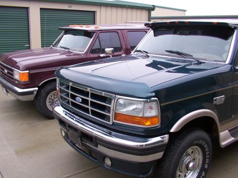 1988 Ford C-350 (Centurion Conversions) - Two Ford F-Series trucks parked in front of storage units, one dark green and one burgundy.