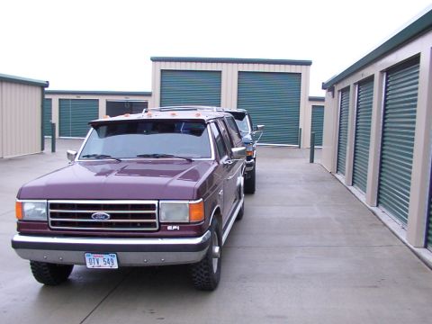 1988 Ford C-350 (Centurion Conversions) - Two Ford F-Series trucks are parked in a row outside storage units.