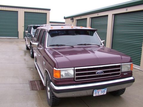 1988 Ford C-350 (Centurion Conversions) - A maroon Ford truck is parked in front of storage units, with another vehicle behind it.