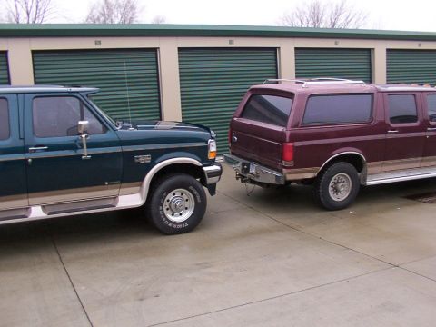1988 Ford C-350 (Centurion Conversions) - Two Ford trucks, a green F-Series and a maroon Bronco SUV, are parked side-by-side in front of storage unit doors.