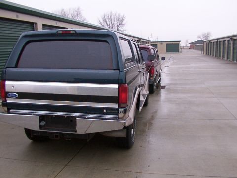 1988 Ford C-350 (Centurion Conversions) - A line of pickup trucks, including a dark green and silver 1988 Ford C-350 Centurion Conversions, are parked outside storage units.