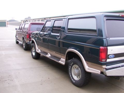 1988 Ford C-350 (Centurion Conversions) - Two Ford Bronco Centurion conversion SUVs are parked side-by-side in front of storage units.