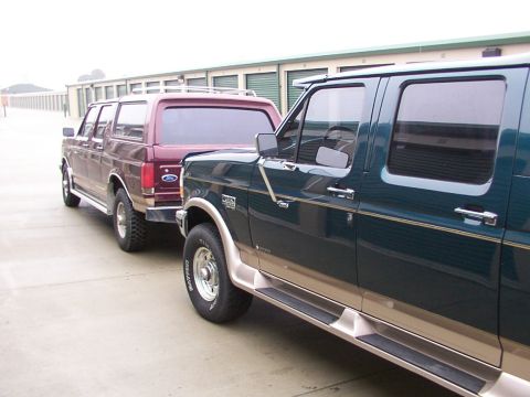 1988 Ford C-350 (Centurion Conversions) - Two Ford trucks, a Bronco and an F-Series, are parked side-by-side in front of storage units.