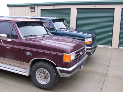 1988 Ford C-350 (Centurion Conversions) - Two Ford trucks, a maroon F-250 and a dark green F-350, are parked in front of storage units.