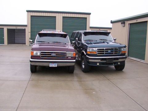 1988 Ford C-350 (Centurion Conversions) - Two Ford trucks are parked in front of storage units on a cloudy day.