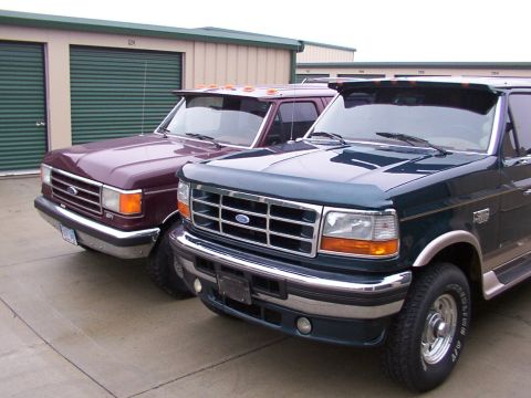 1988 Ford C-350 (Centurion Conversions) - Two Ford trucks, a dark green one in front and a maroon one behind it, are parked outside storage units.