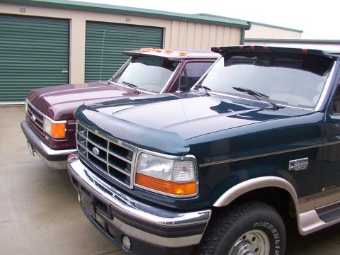 1988 Ford C-350 (Centurion Conversions) - Two Ford trucks are parked side-by-side in front of storage unit doors.