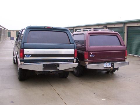 1988 Ford C-350 (Centurion Conversions) - Two Ford Broncos are parked side-by-side in front of storage unit doors.