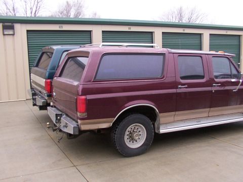 1988 Ford C-350 (Centurion Conversions) - Two trucks are parked in front of storage units, one maroon and one green.