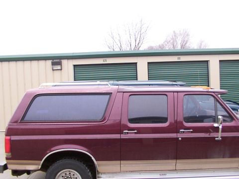 1988 Ford C-350 (Centurion Conversions) - Side view of a maroon van with tan lower body trim and a roof rack parked in front of storage units.