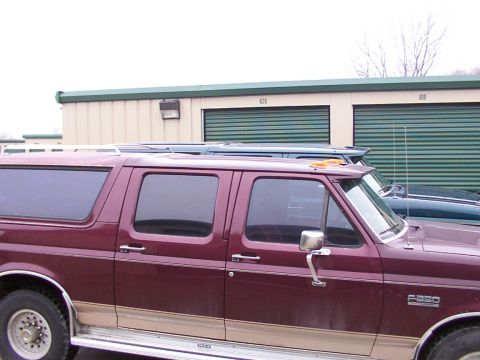1988 Ford C-350 (Centurion Conversions) - Side view of a maroon extended cab pickup truck and a dark blue SUV parked in front of storage units.