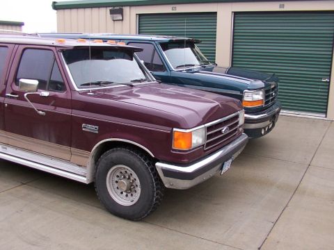 1988 Ford C-350 (Centurion Conversions) - Two Ford trucks, a maroon F-350 and a dark green model, are parked in front of storage units.