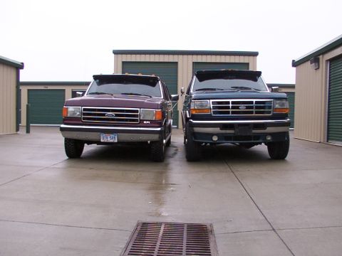 1988 Ford C-350 (Centurion Conversions) - Two Ford trucks are parked in front of storage units on a cloudy day.