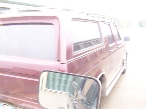 1988 Ford C-350 (Centurion Conversions) - The rear passenger side of a maroon Ford Bronco is visible, parked in front of a garage door.