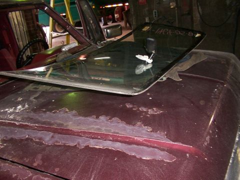 1988 Ford C-350 (Centurion Conversions) - Windshield with handwritten text and a suction cup mount, resting on a maroon car hood with peeling paint.