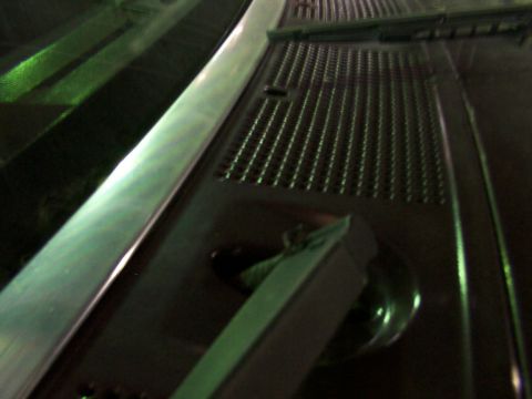 1988 Ford C-350 (Centurion Conversions) - Close-up of a vehicle's windshield wiper mechanism, showing a metal arm and a perforated grate.