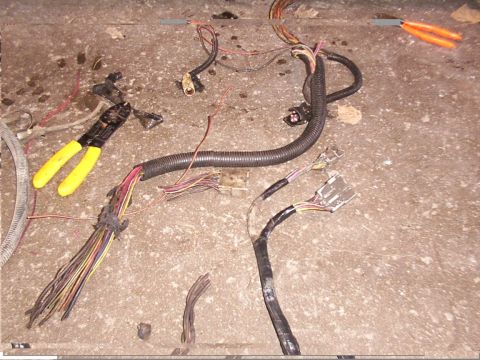1988 Ford C-350 (Centurion Conversions) - A damaged wiring harness lies on a concrete surface alongside wire cutters and pliers, suggesting repair or removal.