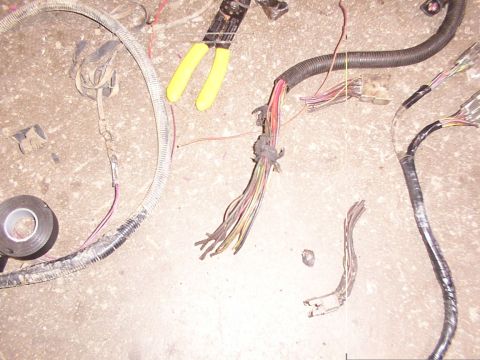 1988 Ford C-350 (Centurion Conversions) - A close-up of a damaged vehicle wiring harness with wire cutters and electrical tape on a concrete surface.