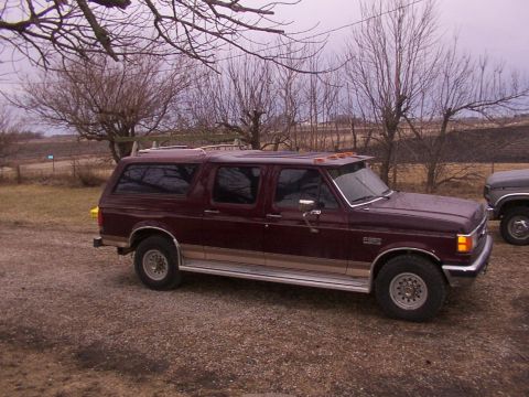1988 Ford C-350 (Centurion Conversions) - Maroon SUV with tan trim parked on gravel, with bare trees and a gray truck in the background.