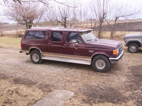 1988 Ford C-350 (Centurion Conversions) - Maroon extended cab pickup truck with a camper shell is parked next to another truck.