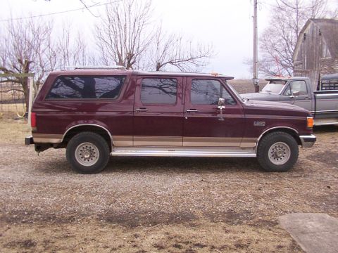 1988 Ford C-350 (Centurion Conversions) - Side view of a maroon extended cab SUV with tan trim, parked next to a gray pickup truck.