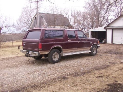 1988 Ford C-350 (Centurion Conversions) - A maroon Ford SUV conversion with tan trim sits parked in a gravel driveway next to a barn and garage.