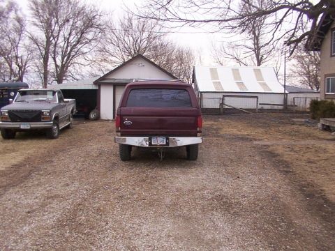 1988 Ford C-350 (Centurion Conversions) - A maroon pickup truck with a camper shell is parked in a gravel lot, with another truck visible to the left.