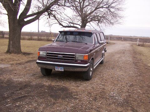 1988 Ford C-350 (Centurion Conversions) - Maroon Ford F-Series truck with a camper shell is parked on a gravel driveway near a tree.