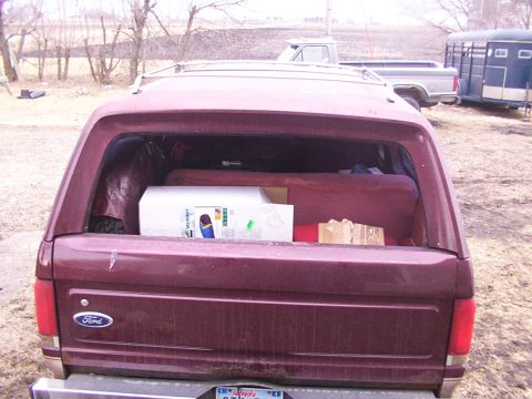 1988 Ford C-350 (Centurion Conversions) - Rear view of a maroon Ford Bronco loaded with items, including a large white box. Other vehicles and a trailer are visible in the backgroun…