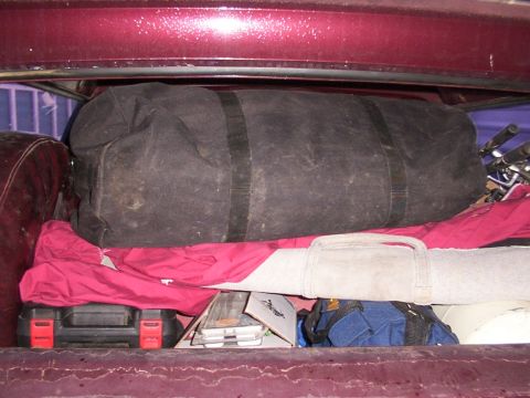 1988 Ford C-350 (Centurion Conversions) - The cargo area of a vehicle is filled with a large duffel bag, red fabric, a tool case, and other assorted items.