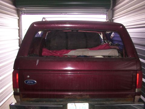 1988 Ford C-350 (Centurion Conversions) - Maroon Ford Bronco parked inside a storage unit, rear view showing cargo area filled with bags and blankets.