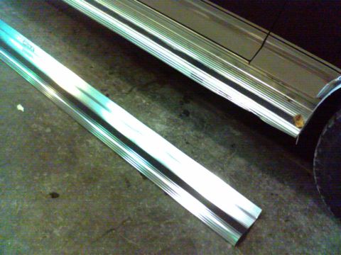 1988 Ford C-350 (Centurion Conversions) - A detached chrome trim piece lies on the ground near the side of a vehicle with extensive silver and black trim.