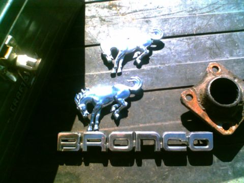 1988 Ford C-350 (Centurion Conversions) - Ford Bronco emblems and a rusty exhaust flange are laid out on a surface.