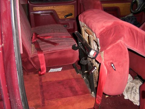 1988 Ford C-350 (Centurion Conversions) - Interior of a van with red velour seats and seatbelts, showing wood paneling on the door.