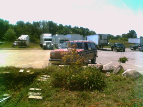1988 Ford C-350 (Centurion Conversions) - A red SUV is parked in a lot with multiple semi-trucks and trailers visible.