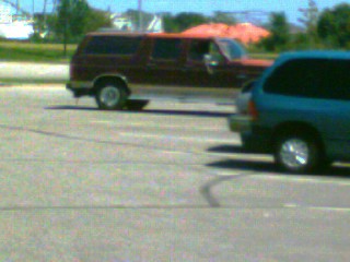 1988 Ford C-350 (Centurion Conversions) - A maroon SUV is seen driving on a road, with another vehicle partially visible in the foreground.