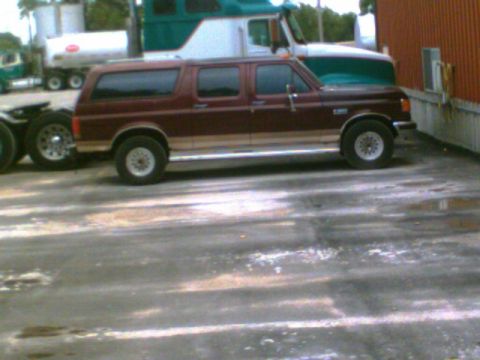 1988 Ford C-350 (Centurion Conversions) - This maroon SUV with tan trim is parked next to a large truck. The vehicle's body style suggests it is from the 1980s.