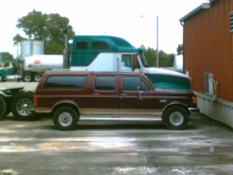 1988 Ford C-350 (Centurion Conversions) - Maroon Ford Bronco Centurion Conversion is parked next to a semi-truck and a building.