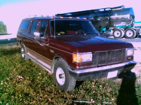 1988 Ford C-350 (Centurion Conversions) - Maroon Ford Econoline conversion van with woodgrain trim is parked on grass, with a semi-trailer truck behind it.