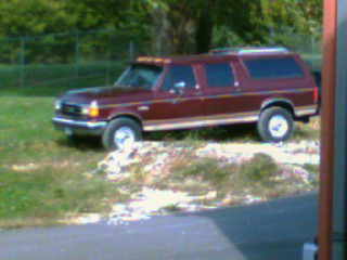 1988 Ford C-350 (Centurion Conversions) - A maroon SUV with wood paneling is parked on a grassy area next to a paved surface.