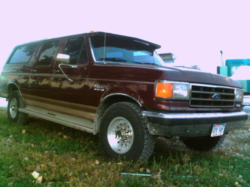 Maroon Ford Bronco with tan side trim, parked on grass. Front 3/4 view
