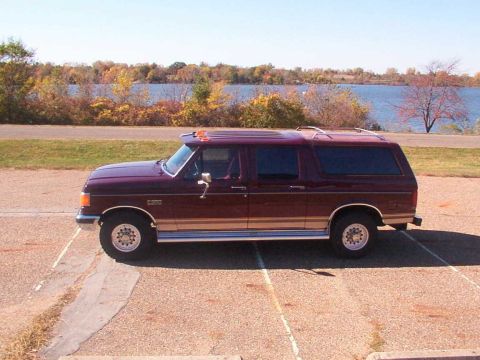 1988 Ford C-350 (Centurion Conversions) - Maroon Ford F-Series SUV conversion parked outdoors with a lake and trees in the background.