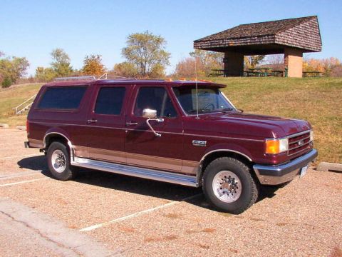 1988 Ford C-350 (Centurion Conversions) - Maroon Ford F-Series SUV conversion with tan trim parked in a gravel lot near a picnic shelter.