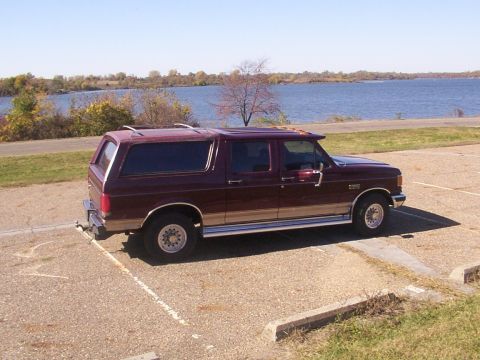 1988 Ford C-350 (Centurion Conversions) - Maroon SUV with tan trim and roof rack parked by a lake on a sunny day.