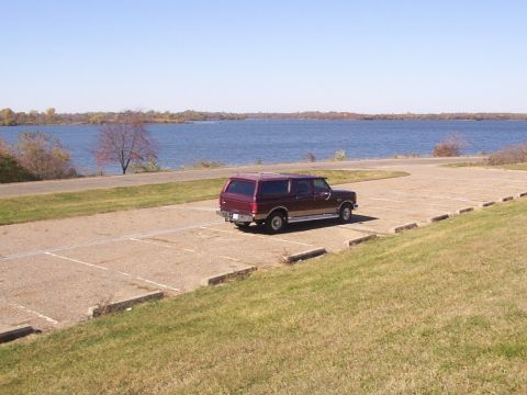 1988 Ford C-350 (Centurion Conversions) - A maroon SUV is parked in a lot with a lake in the background. The vehicle's body style suggests it is from the late 1980s.