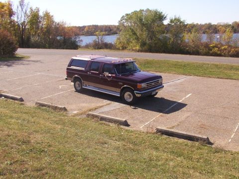 1988 Ford C-350 (Centurion Conversions) - Maroon Ford F-Series truck with camper shell parked in a lot by a lake.