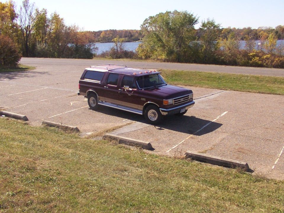 Maroon Ford F-Series truck with a camper shell parked in a lot near a body of water