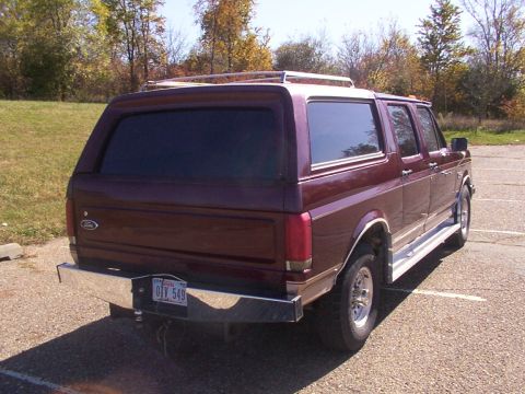 1988 Ford C-350 (Centurion Conversions) - Maroon Ford Bronco SUV seen from the rear, parked outdoors with trees in the background.