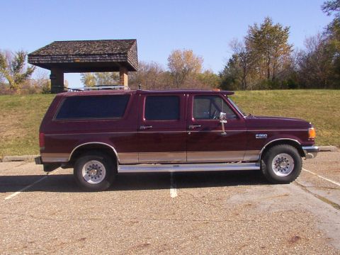 1988 Ford C-350 (Centurion Conversions) - A maroon SUV with tan lower trim and chrome wheels is parked in a lot next to a picnic shelter.