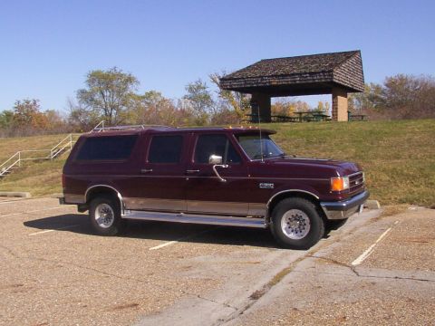 1988 Ford C-350 (Centurion Conversions) - Maroon SUV with chrome trim and roof rack parked in a lot near a picnic shelter.